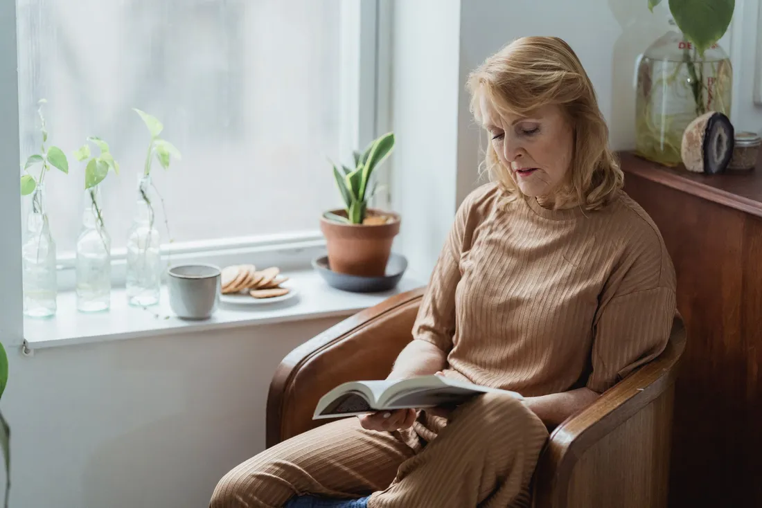 Femme âgée lisant un livre dans un fauteuil près de la fenêtre