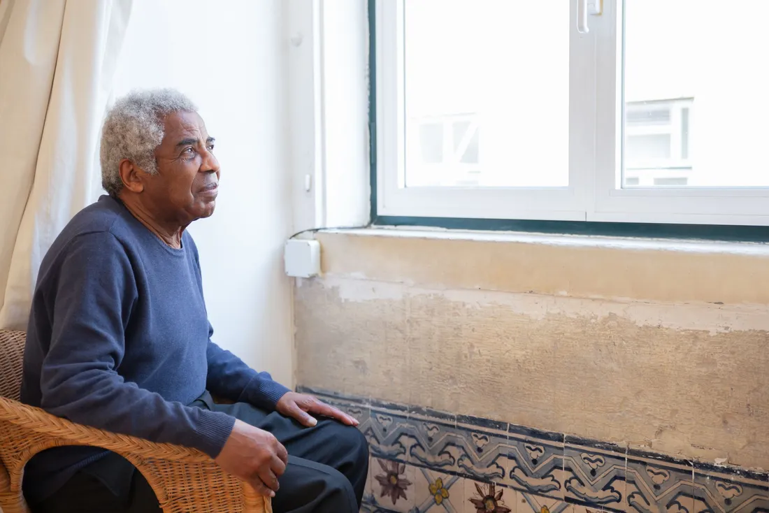 Homme âgé assis près de la fenêtre de son salon
