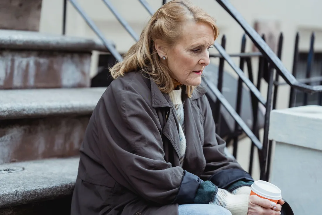 Femme âgée assise sur les marches extérieures, une tasse à la main