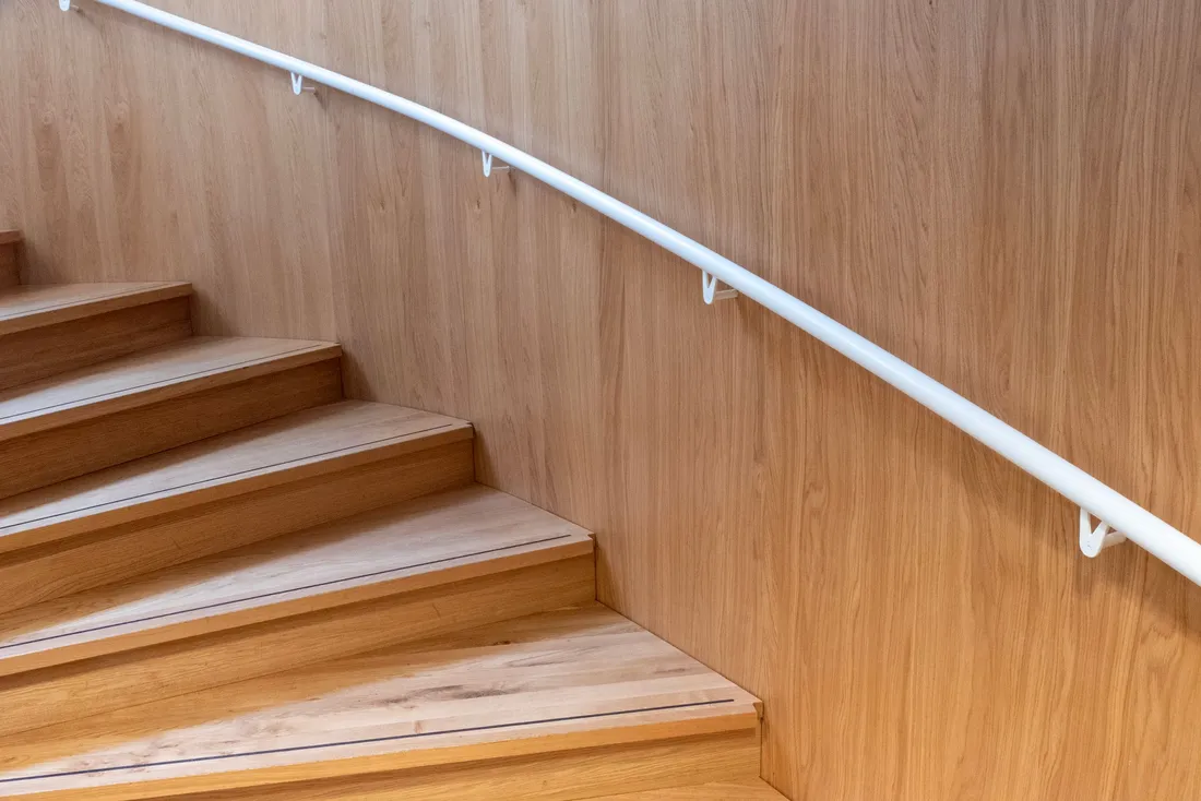 Escalier tournant en bois clair longé d'une main courante blanche qui épouse la courbe du mur